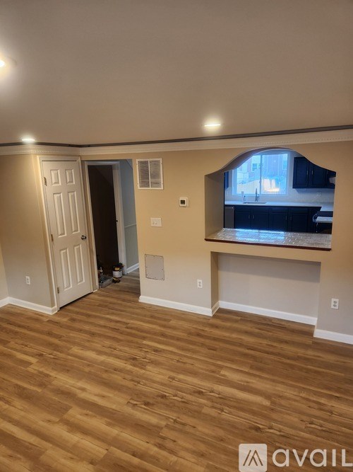 A room with wooden flooring and a window overlooking a kitchen.