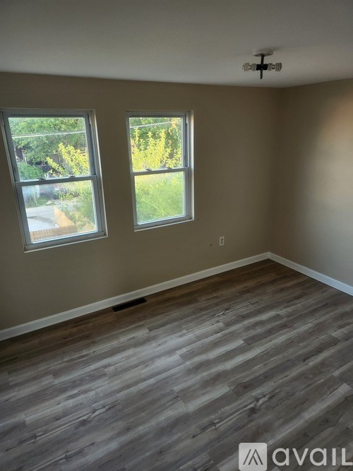 A room with wooden flooring and two windows.