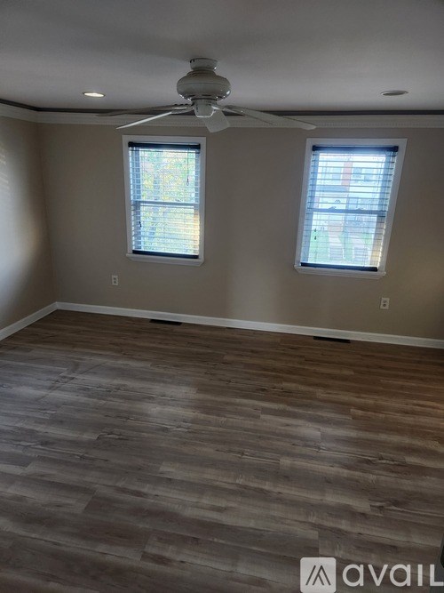 A room with wooden flooring and two windows.