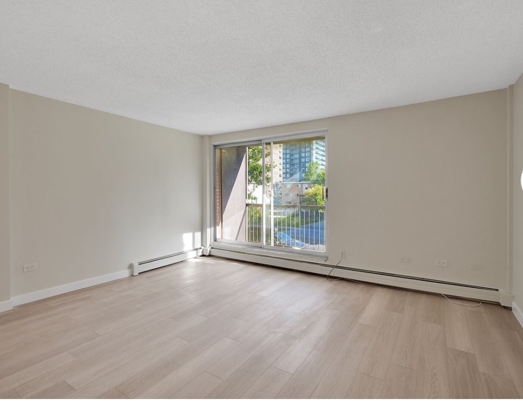 Empty room with wooden flooring and a window overlooking a pool.
