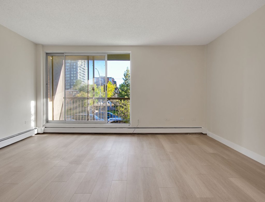 A room with a sliding glass door leading to a balcony with a view of a blue car and trees.