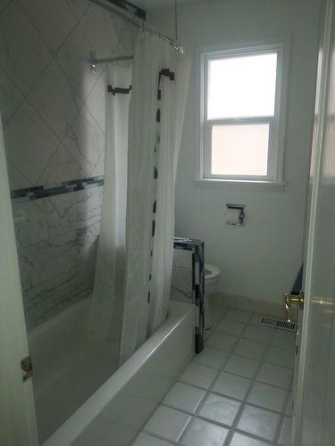 A white bathroom with a marble wall and a window.