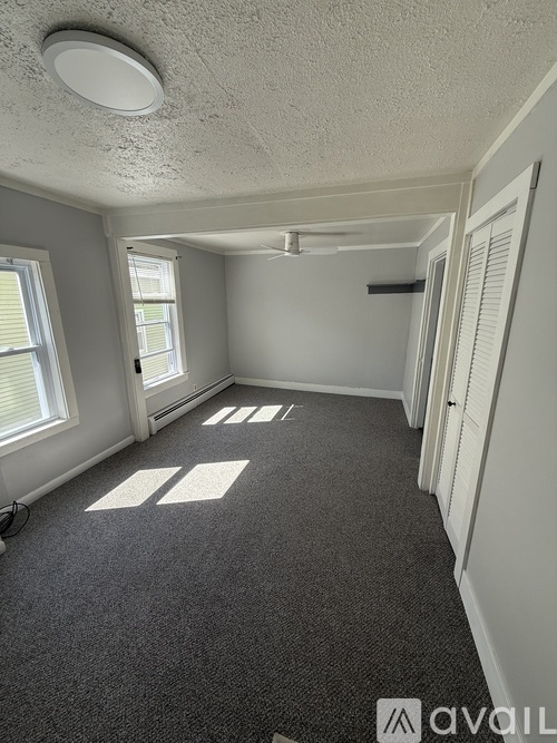 A room with a fan on the ceiling and a window with a view of trees and a car outside.