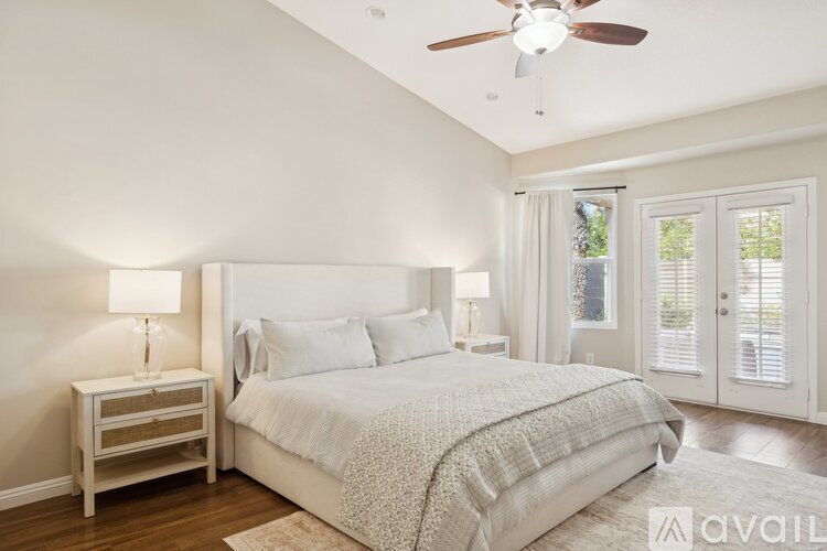 A bedroom with a large bed, a nightstand with a lamp, and a ceiling fan.