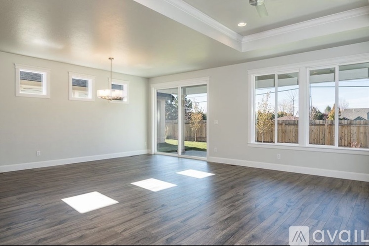 A spacious room with wooden floors and a large window overlooking a fence.