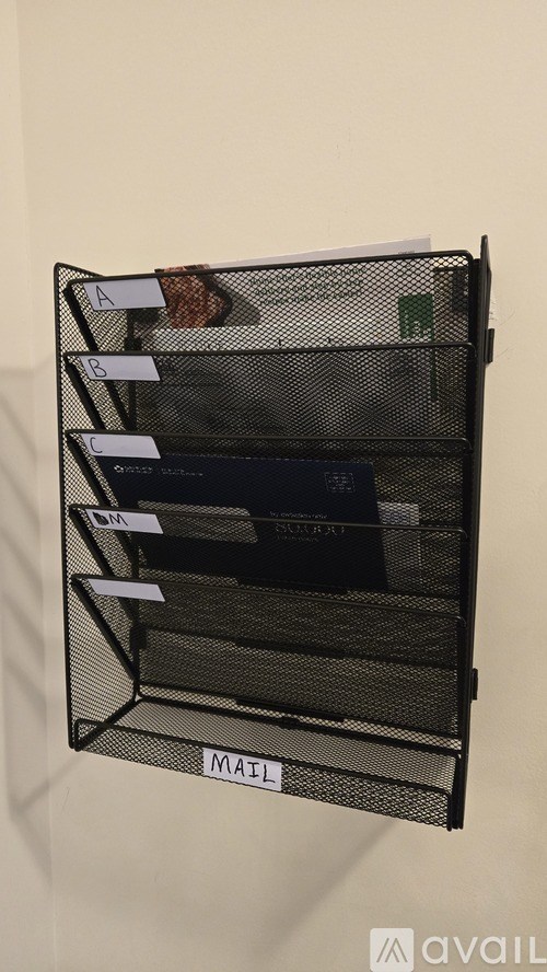 A black wire mesh file organizer with labels A, B, C, and MATERIAL hanging on a wall.