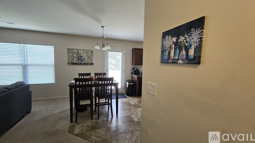 A dining room with a table set for six and a painting on the wall.