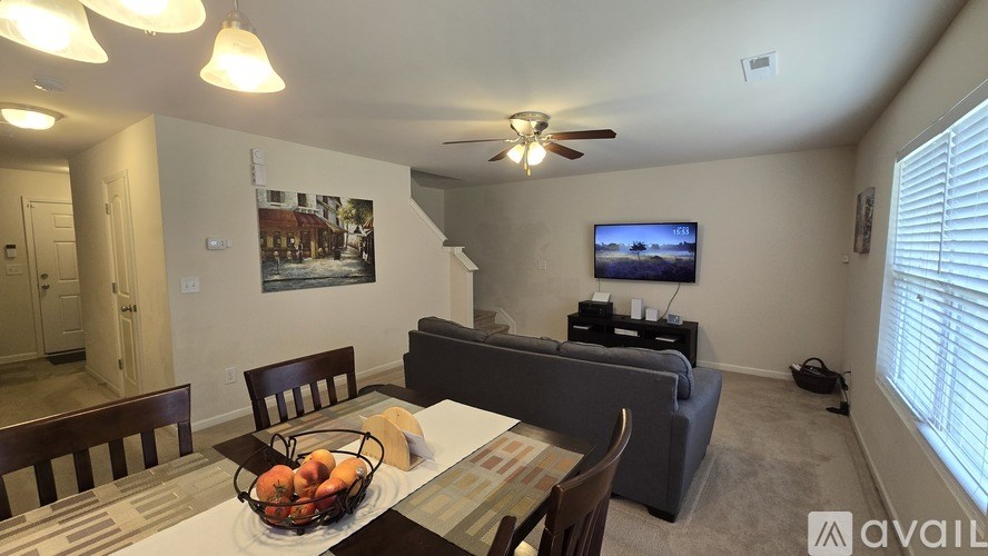 A living room with a couch, a dining table with chairs, a television, and a painting on the wall.