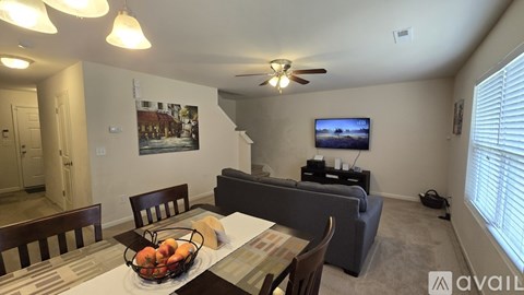 A living room with a couch, a dining table with chairs, a television, and a painting on the wall.