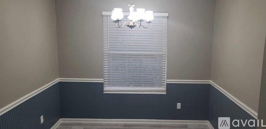 A room with a window covered in blinds and a chandelier hanging from the ceiling.