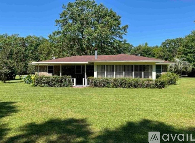 A house with a red roof and white trim is surrounded by a green lawn and trees.