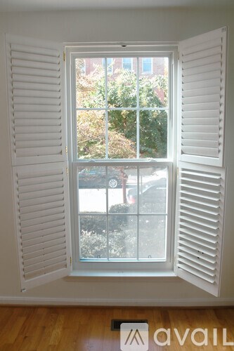 A window with white shutters and a view of a backyard.