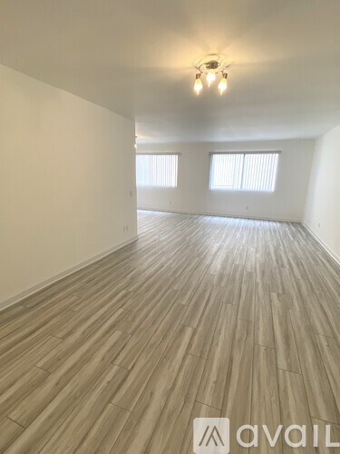 A room with wooden flooring and two windows.