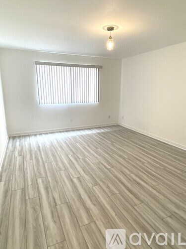 A room with wooden flooring and a window with blinds.