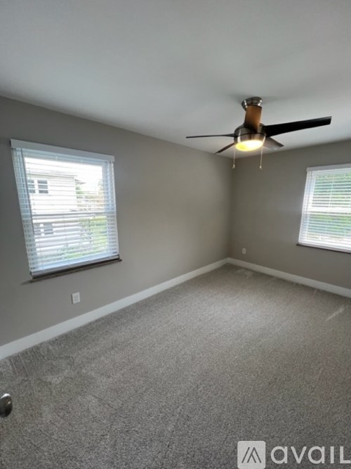 A room with a ceiling fan and two windows.