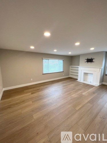 A spacious room with wooden flooring and a fireplace.