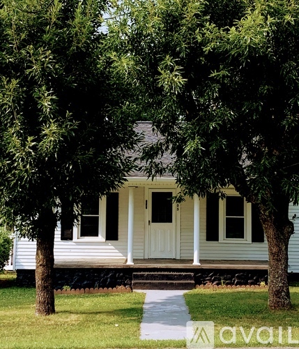 A white house with a porch and a tree in front.