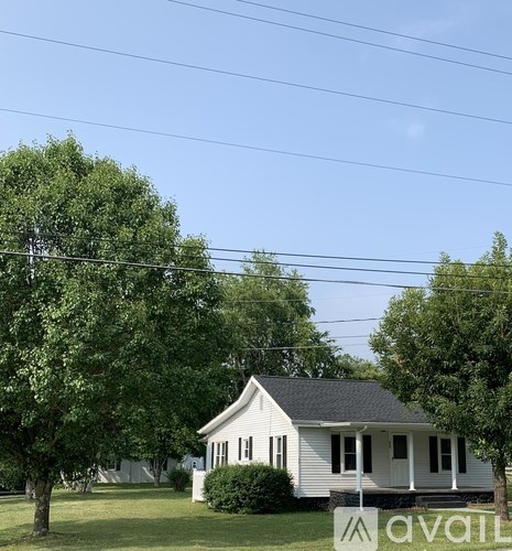 A white house with a black roof is surrounded by green trees.