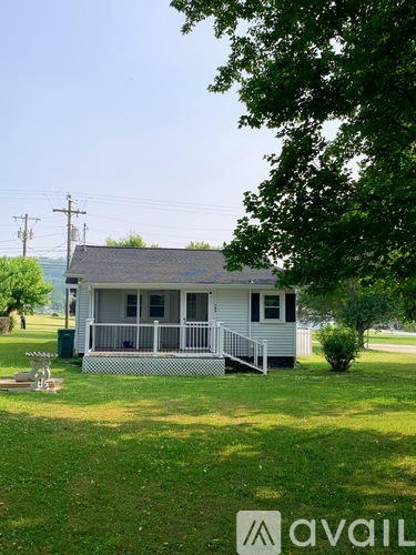 A small house with a porch and a tree in front.