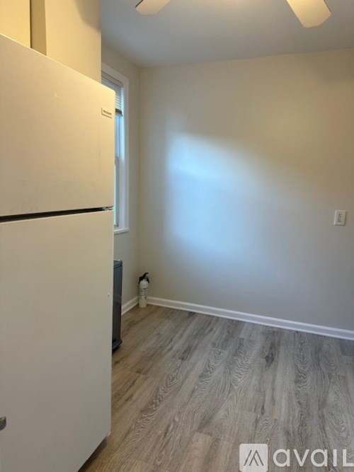 A white refrigerator in a room with light wood flooring and a window.