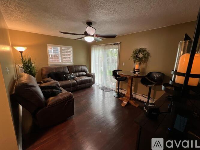 A living room with a brown leather couch and a ceiling fan.