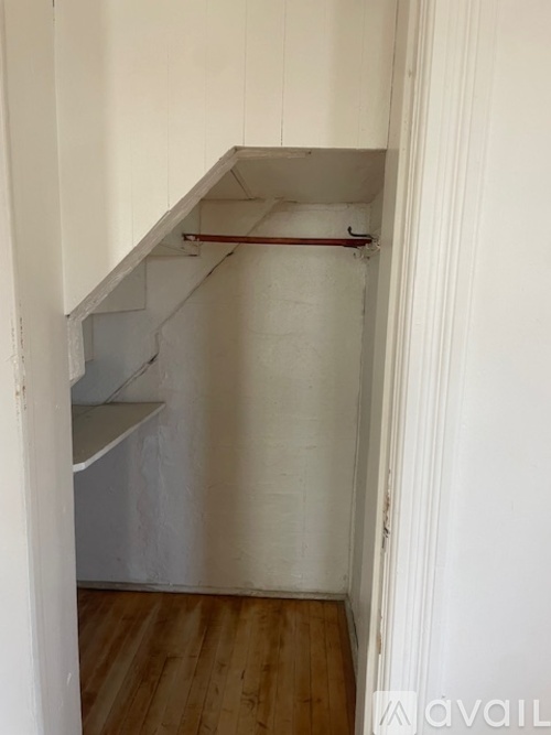 A white wall with a pipe and a white shelf.