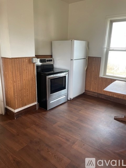 A kitchen with a white fridge, black stove and oven, and wooden floors.