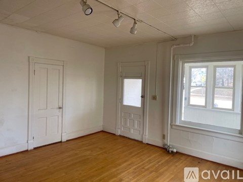 A room with a wooden floor, white walls, and a window with a view of trees outside.