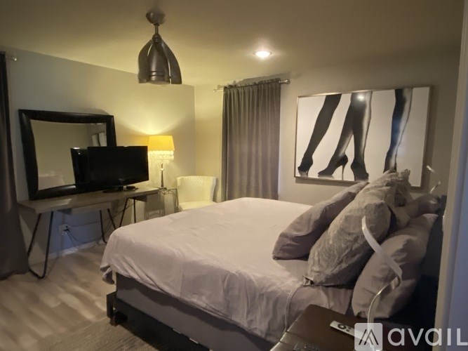 A bedroom with a bed, a television, a mirror, a lamp, and a painting.