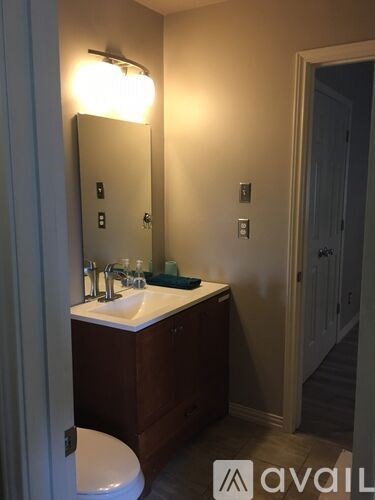 A bathroom with a toilet, sink, mirror and light switches.