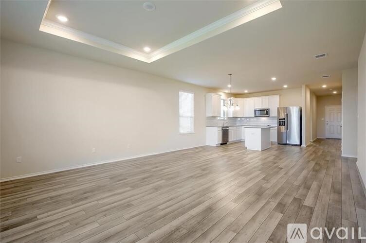 A spacious living room with wooden flooring and a kitchen area in the background.