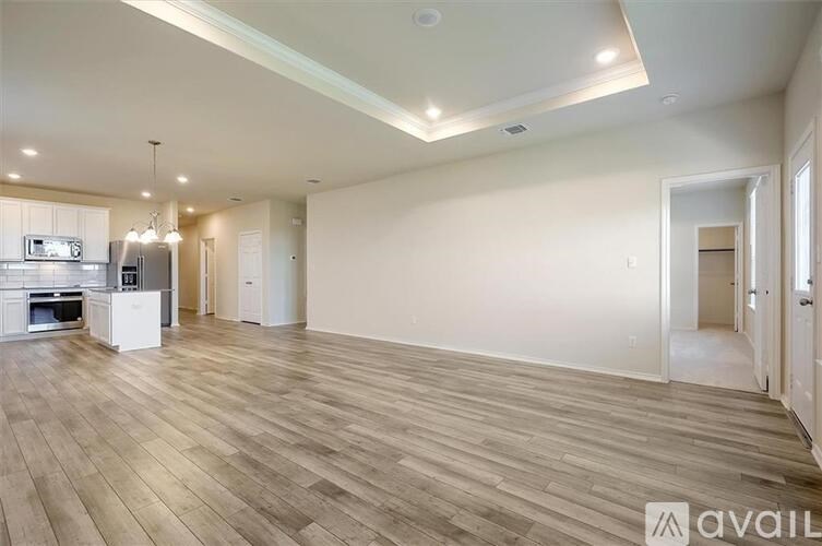 A spacious living room with wooden flooring and a kitchen area in the background.