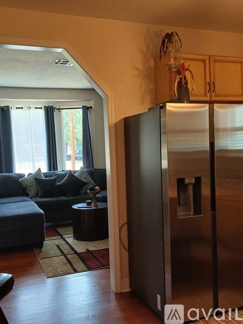 A modern kitchen with a stainless steel refrigerator and a living room with a grey couch and a small table.