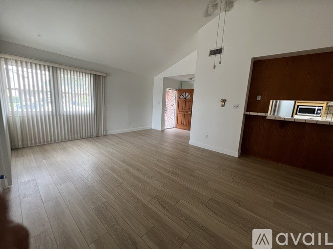 A spacious room with wooden flooring and a large window with blinds.