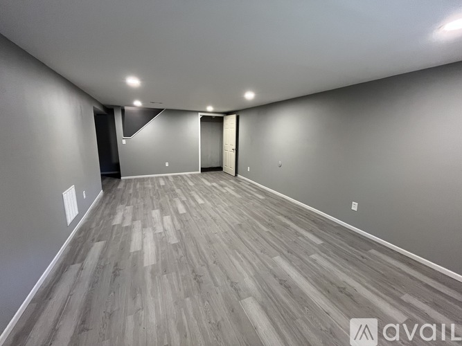 A spacious room with wooden flooring and white walls.