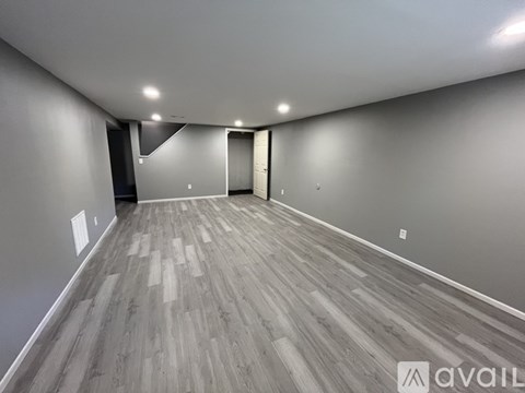 A spacious room with wooden flooring and white walls.