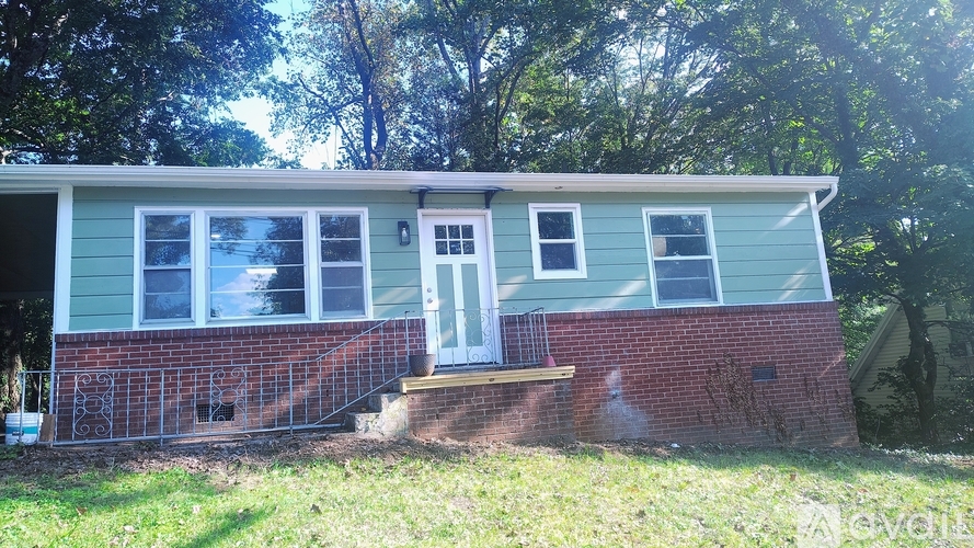 A small house with a white door and windows is surrounded by trees.