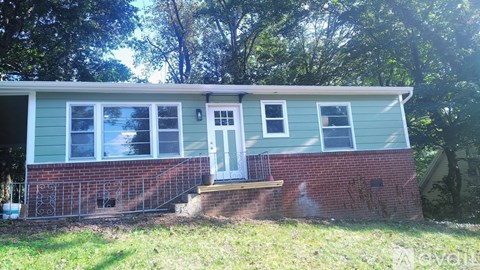 A small house with a white door and windows is surrounded by trees.