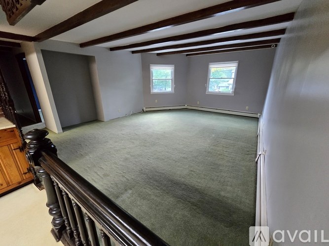 A large, empty room with a carpeted floor and wooden beams on the ceiling.