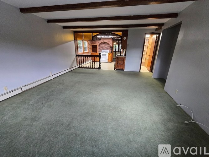 A spacious room with a grey carpet and white walls, featuring a balcony with a railing and a view of a brick building.