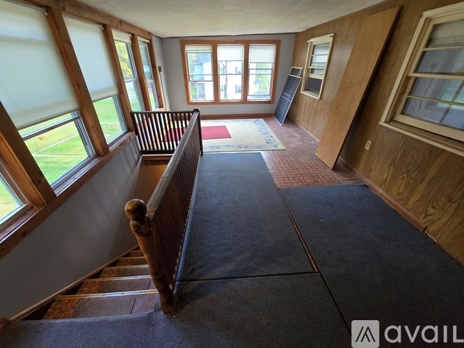 A wooden staircase leads to a bright room with large windows.