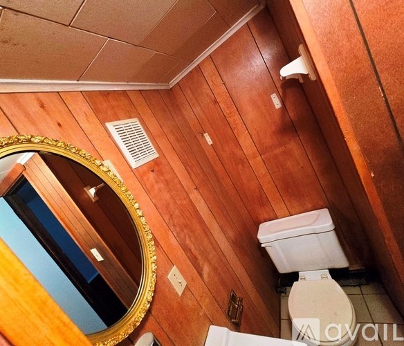 A bathroom with a toilet, a mirror, and a wooden wall.