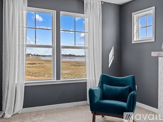 A room with a green armchair and a view of a field through the windows.