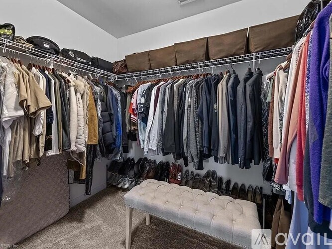 A walk in closet with clothes hanging and a bench.