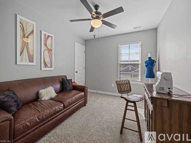 A living room with a brown leather couch, a ceiling fan, and a wooden chair.