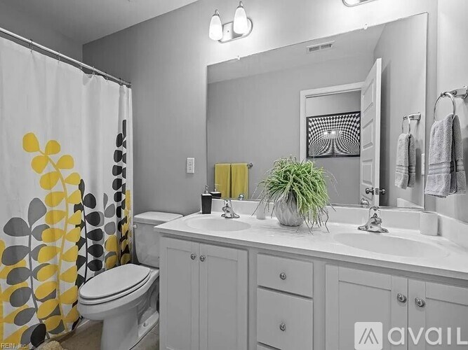 A bathroom with a white toilet, a sink with a potted plant on it, and a shower curtain with yellow circles.