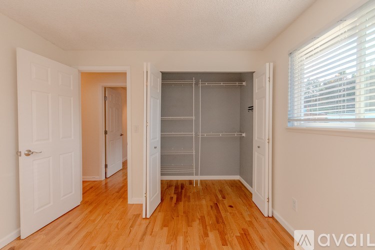 A room with a white door, a wooden floor, and a white wall with a window.