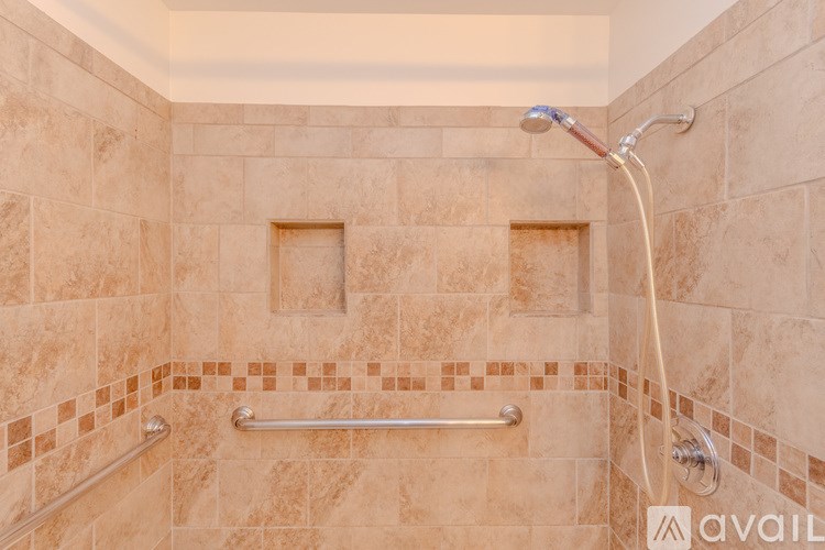 A tiled shower with a glass door and a grab bar.