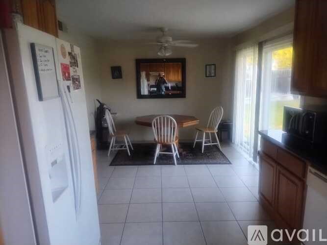 A kitchen with a white fridge, a dining table with chairs, and a ceiling fan.