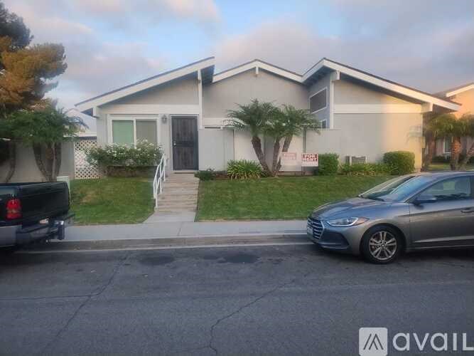 A grey car is parked in front of a house with a sign that says "For Sale".